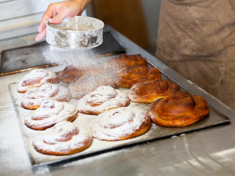 A person pouring powdered sugar on a tray full of salad